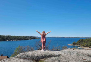 Personne debout bras levés sur un rocher face à l’eau près de Sävö Bed and Breakfast Glampingtenten Södermanland.