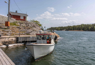 Barco atracado junto a cabaña roja en orilla rocosa, Sävö Bed and Breakfast, glamping en Södermanland.