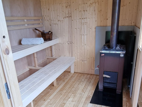 Indretning af en træsauna med bænke, håndklæde, spand og brændeovn på Sävö Bed and Breakfast Glamping.