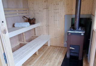 Indretning af en træsauna med bænke, håndklæde, spand og brændeovn på Sävö Bed and Breakfast Glamping.