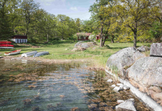 Scenic glamping site by the lake with boats, green grass and cabins at Sävö Bed and Breakfast, Södermanland.