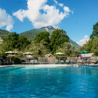 Piscine extérieure avec transats et parasols au Huttopia Vallouise - Glamping Hautes-Alpes, entourée de montagnes.