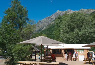 Buitenruimte met banken, parasols en een paraglider boven Huttopia Vallouise, Hautes-Alpes.