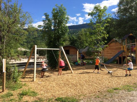 Kinderen spelen op de speeltuin van Huttopia Vallouise - Glamping Hautes-Alpes, omgeven door houten huisjes.