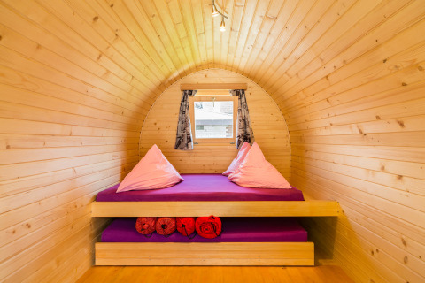 Knusse houten iglo van binnen met paars bed en kussens, glamping op Camping Lazy Rancho in Zwitserland.