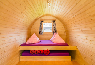 Interior view of a cozy wooden igloo with purple bedding and pillows, glamping at Camping Lazy Rancho.