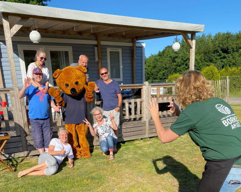 Familie tager gruppefoto med bjørnemaskot foran luksuscampinghytte på Luxe Camping Borken am See.