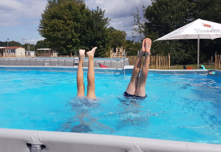 Twee kinderen doen een handstand in het zwembad bij Luxe Camping Borken am See - Glamping Noordrijn-Westfalen, omringd door groen.