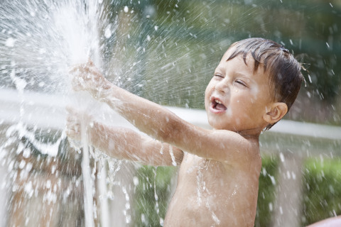 Un niño alegre juega con agua de una manguera en Luxe Camping Borken am See - Glamping Noordrijn-Westfalen.