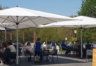 Terrazza esterna di Luxe Camping Borken am See - Glamping Noordrijn-Westfalen con ospiti sotto grandi ombrelloni.