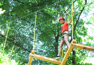 Kind auf einem Kletterparcours mit Sicherheitsgurt und Helm bei Luxe Camping Borken am See - Glamping Nordrhein-Westfalen.