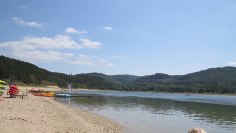 Lakeside beach with canoes and kayaks, green hills, and glamping site at Nature's Pace Holidays Occitanie.