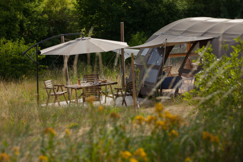 Nature’s Pace Holidays - Glamping Occitanie: Luxurious tent, wooden deck and umbrella in wild nature.