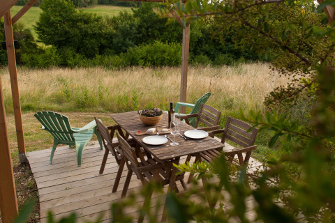 Mesa y sillas de madera en terraza exterior en Nature's Pace Holidays - Glamping Occitanie rodeado de naturaleza.