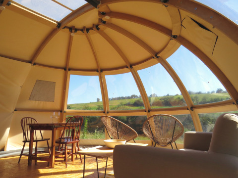 Vue intérieure d’un dôme de glamping Nature’s Pace Holidays avec mobilier et belle vue sur la campagne.