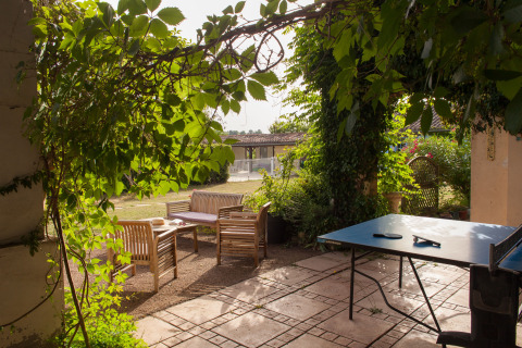 Shaded outdoor patio with wooden seating and ping pong table at Nature's Pace Holidays - Glamping Occitanie.