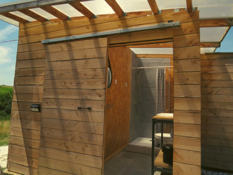 Cabina glamping all'aperto con pannelli di legno e porta scorrevole, bagno moderno, Nature's Pace Holidays.