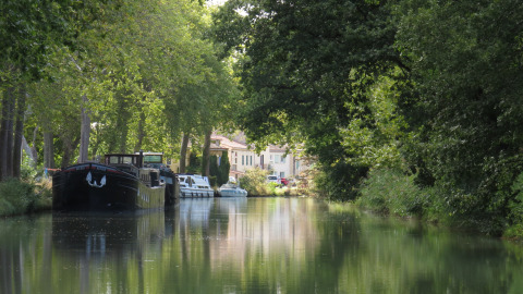 Barcos atracados en un canal rodeado de árboles cerca de Nature's Pace Holidays - Glamping Occitanie.