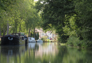 Boten aangemeerd aan een rustige, boomrijke kanaal bij Nature's Pace Holidays - Glamping Occitanie.