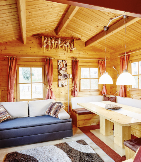 Gemütliche Holzhütte mit Sitzbereich und Esstisch bei Camping Dreiländereck - Lodge & Wijnvat Tirol.