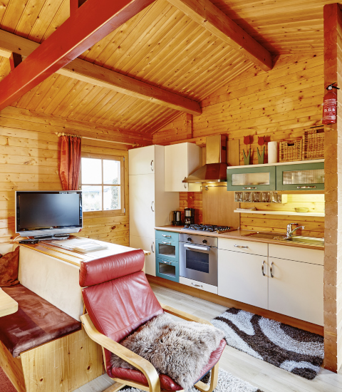 Gemütliches Holzlodge-Interieur mit moderner Küche und rotem Sessel bei Camping Dreiländereck Tirol.