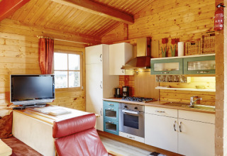 Cozy wooden lodge with modern kitchen and red armchair at Camping Dreilandereck Lodge & Wijnvat Tirol.