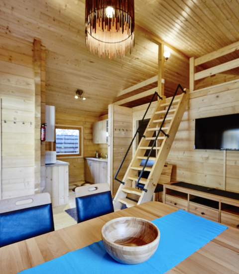 Interior view of a glamping lodge featuring wooden decor, dining table, loft stairs, and modern amenities.