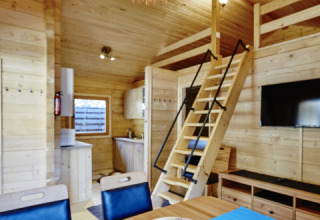 Interieur van een glamping lodge met houten inrichting, eettafel, trap naar de loft en moderne voorzieningen.