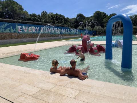 Famiglia rilassata presso la piscina per bambini con giochi d'acqua al Park Mas Patoxas – Costa Brava.