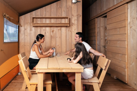 Family spending time at a wooden table inside glamping accommodation at Park Mas Patoxas, Costa Brava.