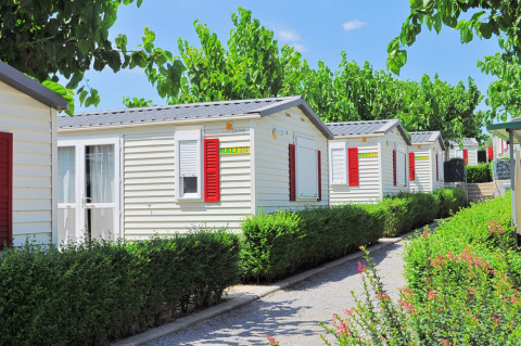 Fila de bungalows móviles con contraventanas rojas rodeados de vegetación en Park Mas Patoxas – Bungalows Costa Brava.