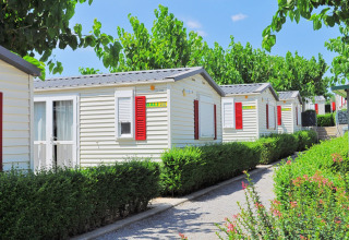 Rangée de bungalows mobiles avec volets rouges entourés de verdure au Park Mas Patoxas – Bungalows Costa Brava.