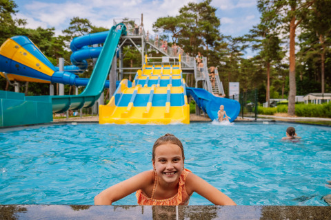 Meisje in het zwembad voor kleurrijke glijbanen bij Camping Samoza – Glamping Lodges Veluwe in het bos.