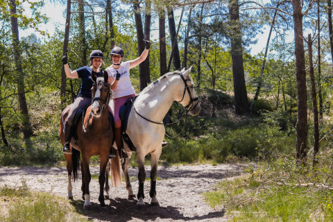 Twee blije vrouwen te paard in een zonnig bos bij Camping Samoza – Glamping Lodges Veluwe, Nederland.