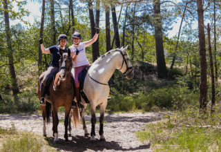 Due ragazze felici a cavallo in una foresta soleggiata vicino a Camping Samoza – Glamping Lodges Veluwe, Paesi Bassi.