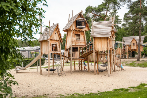 Estructuras de juego de madera en Camping Samoza – Glamping Lodges Veluwe, rodeadas de árboles y naturaleza.