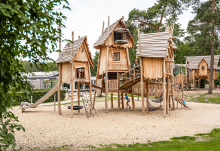 Spielplatz mit Holzspielhäusern und Rutsche bei Camping Samoza – Glamping Lodges Veluwe, umgeben von grüner Natur.
