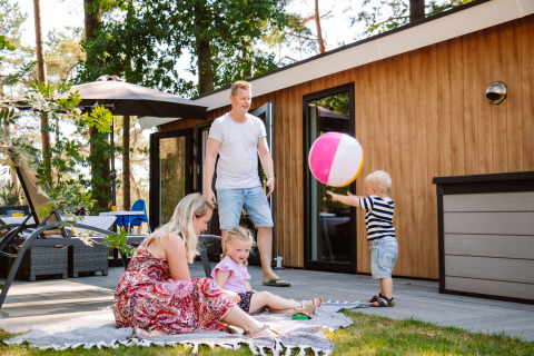 Gezin speelt en ontspant buiten bij een houten lodge op Camping Samoza – Glamping Lodges Veluwe in het bos.