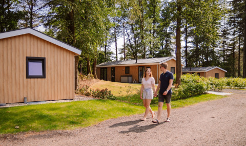 Paar spaziert vor modernen Glamping-Lodges im Wald bei Camping Samoza – Glamping Lodges Veluwe.