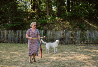Mujer juega con un perro en un campo de césped cerca de la valla en Camping Samoza – Glamping Lodges Veluwe.