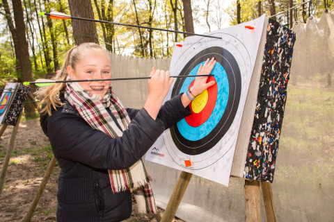 Smiling girl removes arrows from archery target at Camping Samoza – Glamping Lodges Veluwe in the forest