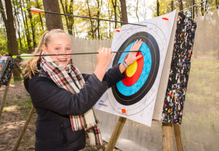 Smiling girl removes arrows from archery target at Camping Samoza – Glamping Lodges Veluwe in the forest