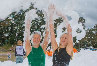 Twee jongeren hebben plezier bij een schuimfeest op Camping Samoza – Glamping Lodges Veluwe, omringd door natuur.