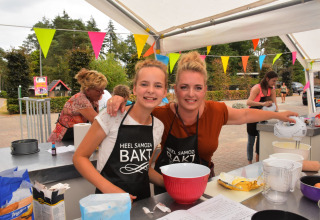 Dos mujeres participan en un concurso de repostería al aire libre en Camping Samoza – Glamping Lodges Veluwe con banderines.