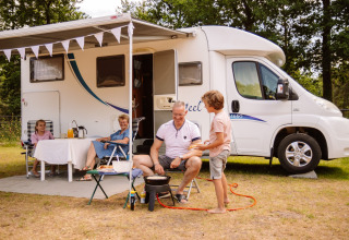 Familie nyder udendørs måltid foran campingvogn på Camping Samoza – Glamping Lodges Veluwe, Holland.