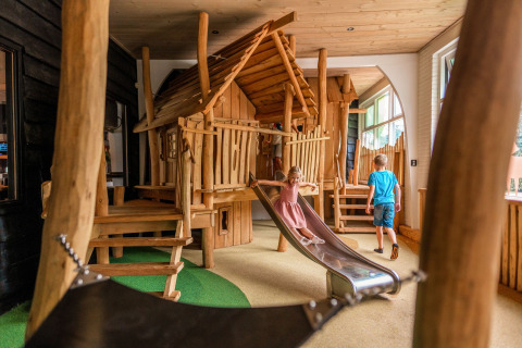 Niños juegan en una cabaña de madera con tobogán en el interior de Camping Samoza – Glamping Lodges Veluwe.