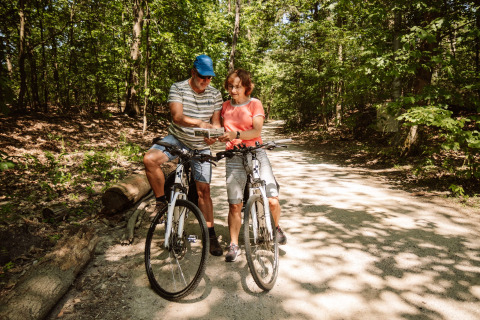 Dos ciclistas adultos se detienen en el bosque para mirar un mapa, glamping cerca de Camping Samoza, Veluwe.