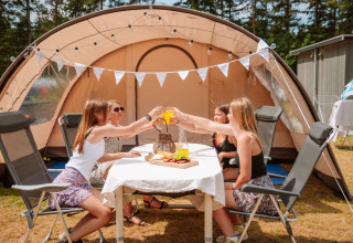 Four women enjoy glamping at a table with food and drinks in front of a tent at Camping Samoza – Glamping Lodges Veluwe.