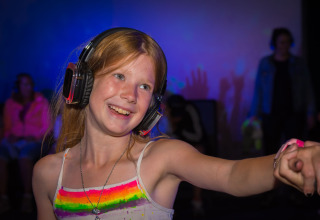 Jeune fille joyeuse avec casque participe à une silent disco au Camping Samoza – Glamping Lodges Veluwe.