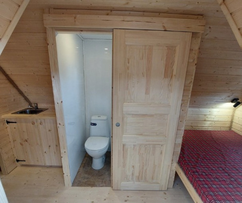 Binnenzicht van glampinghuisje met toilet, wasbak en bed bij Camping Rissbach - Sprookjeshuis Rijnland-Palts.